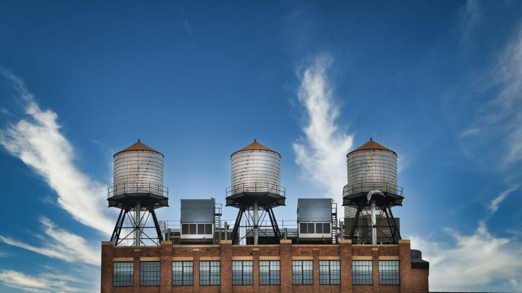 three metal water tanks on top of a brick building with blue sky and white clouds